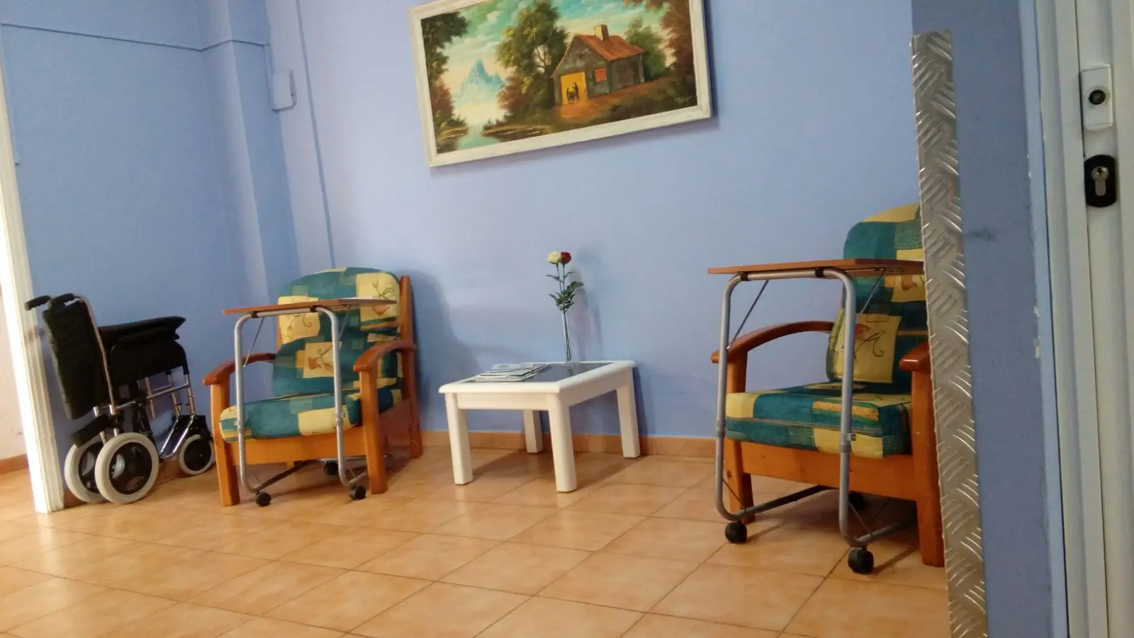 Sala de espera con sillones geriátricos, mesa auxiliar y silla de ruedas