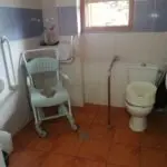 Baño geriátrico con silla de ducha, asideros y espacio de maniobra